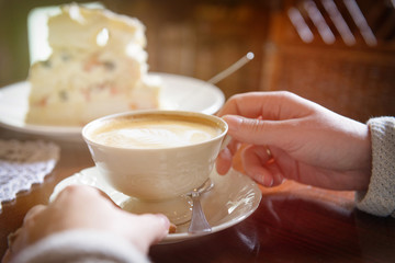 woman's hand holding cappuccino cup in the cafe
