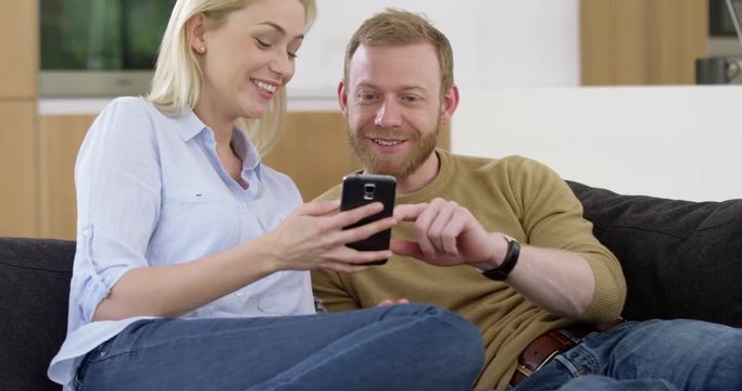 Attractive woman shows photos to handsome boyfriend on smartphone, in slow motion