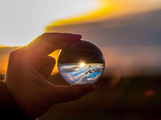 One person with a crystal ball in their hand, reflecting a landscape at sunset and sun reflection