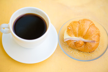 A cup of Black coffee with Ham and cheese croissant