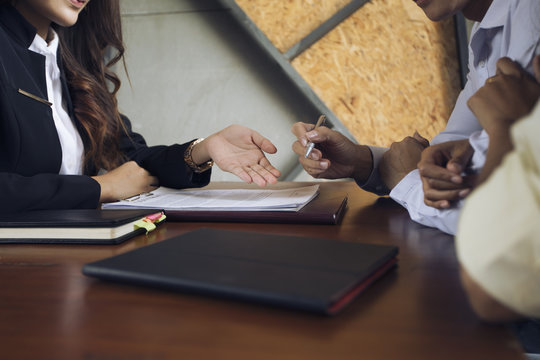 The beautiful financial woman pointing fingers to male and female customers sign a contract in the office on a wooden table. The concept of home loan agreement