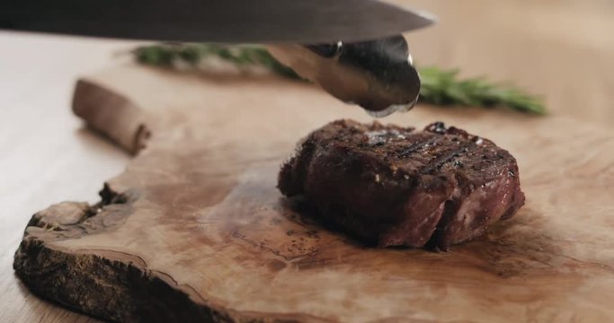 Slow motion slide slicing medium rare fillet mignon steak on wood board