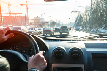 Hands on the steering wheel. View of the road in the city through the windshield of the car