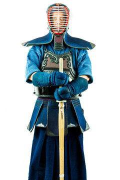 Male wearing a kendo armor with helmet and gloves holding a bamboo sword, standing position.