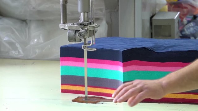 Colored fabrics. Circumcision of the lackeys. Knife on the machine. Men's hand. Factory for tailoring. Close up.