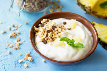 Homemade healthy breakfast in a bowl with homemade baked granola, fresh pineapple and yogurt on a turquoise stone or concrete table. Copy space.