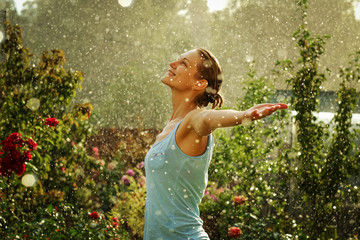 Portrait of a beautiful happy woman enjoying tropical rain falling on her in an exotic garden. - obrazy, fototapety, plakaty