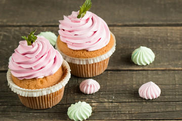 Closeup of cupcakes with vanilla, berries, pink and white cream, chocolate and sprinkles on wooden background. Selective focus. Sweet dessert tasty food concept muffin.