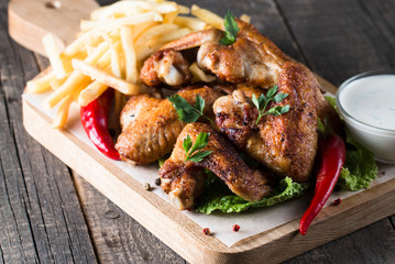Close-up photo of bbq chicken wings with fries and beer. Barbeques meat with sauces, ketchup, mayonnaise. Fast and junk food concept. 