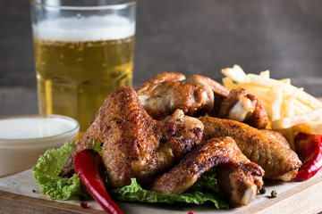 Close-up photo of bbq chicken wings with fries and beer. Barbeques meat with sauces, ketchup, mayonnaise. Fast and junk food concept. 