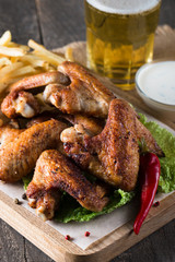 Close-up photo of bbq chicken wings with fries and beer. Barbeques meat with sauces, ketchup, mayonnaise. Fast and junk food concept. 