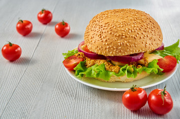 Homemade vegetarian burger with salad, onion rings, cheese, cherry tomatoes and mustard on the gray concrete background with free copy space. Classic american veggie food