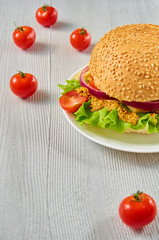 Veggie burger with salad, onion rings, cheese, cherry tomatoes and mustard on the gray concrete background with free copy space. Classic american vegetarian burger. Side view