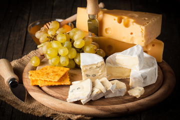 Slate board with various cheese and a glass of red rose wine. Brie. Camembert. Gouda, Masdaam, Roquefort, Cheddar and grapes on a wood with nuts, honey, crackers, blue cheese. Italian, French cheese.
