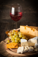 Slate board with various cheese and a glass of red rose wine. Brie. Camembert. Gouda, Masdaam, Roquefort, Cheddar and grapes on a wood with nuts, honey, crackers, blue cheese. Italian, French cheese.