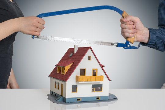 Divorce and dividing a house concept. Man and woman are splitting model of house with saw.