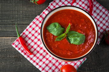 Chili tomato soup with sour cream sauce, cottage cheese, basil and red hot peppers on wooden background. Healthy, vegan and dieting lunch and dinner concept.