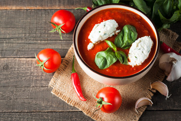 Chili tomato soup with sour cream sauce, cottage cheese, basil and red hot peppers on wooden background. Healthy, vegan and dieting lunch and dinner concept.