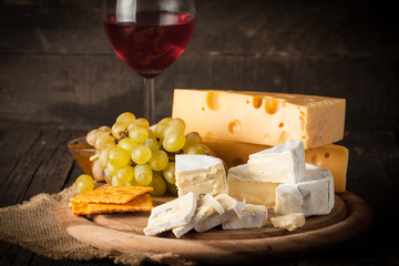 Slate board with various cheese and a glass of red rose wine. Brie. Camembert. Gouda, Masdaam, Roquefort, Cheddar and grapes on a wood with nuts, honey, crackers, blue cheese. Italian, French cheese.