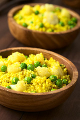 Curried couscous with peas, cauliflower, ginger and garlic served in wooden bowls, photographed with natural light (Selective Focus, Focus in the middle of the first dish)