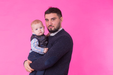 Happy father holding baby son in hands over pink background