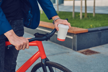 A stylish man holds a cup of coffee while sitting on a bicycle.