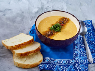 Porcelain bowl of pumpkin soup on napkin over white textured background, close-up, selective focus, top view.