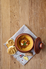 Clay pot of pumpkin soup on homespun napkin rustic wooden background, close-up, selective focus, top view.