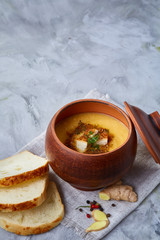 Clay pot of pumpkin soup on homespun napkin rustic wooden background, close-up, selective focus, top view.