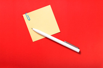 Colored sticker for note, pen, paper clip on red background