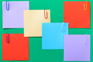 Multicolored stickers for notes, paper clips on green background