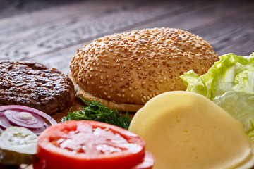 Yummy hamburger ingredients artistically organized on wooden plate, close-up, top view, selective focus