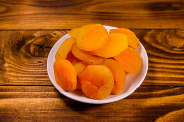 Ceramic plate with dried apricots on wooden table
