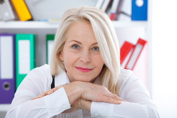 Lovely middle-aged blond woman with a beaming smile sitting at office looking at the camera