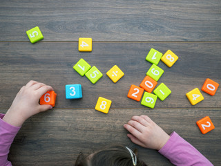 Child playing with numbers on dark wooden background. Directly above.