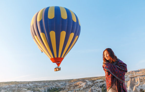 A tourist girl on a mountain top enjoying wonderful view of the sunrise and balloons in Cappadocia. Happy Travel in Turkey concept