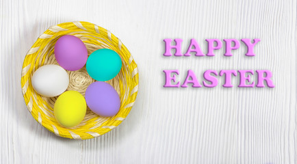 Easter eggs in a basket on a white wooden background. Text of a happy Easter.