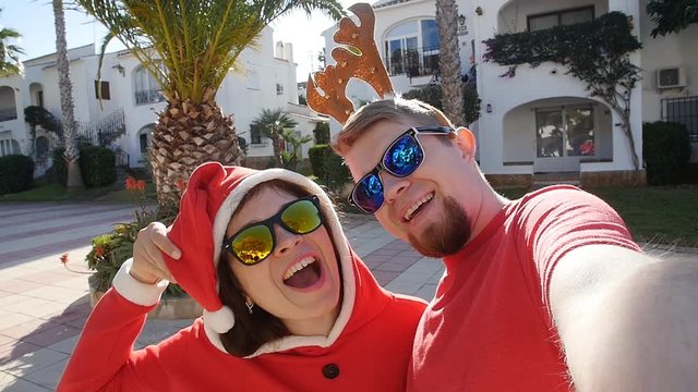 Happy couple in santa hats taking selfie picture from hands in summer outdoors