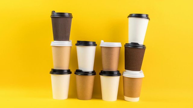 A lot of disposable cups for coffee and tea change places. Nice catering for a coffee shop. Video footage stop motion timelapse. Fun mood. Bright yellow background