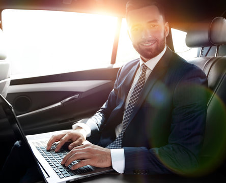 Businessman working on laptop keyboard sitting in car