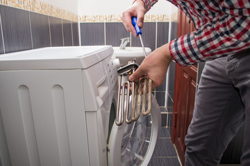 a young repairman with a screwdriver repairs an old heating element or a teng from a faulty washing machine. Washing machine repair