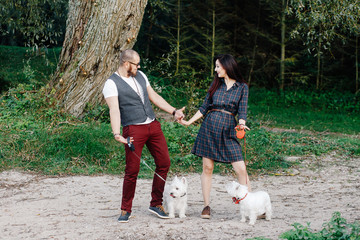 A guy with a girl is walking in the woods of two white dogs