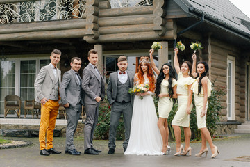 stylish newlyweds along with guests at the wedding stand outside in a rainy day