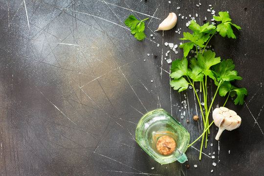 Ingredients for cooking on a dark stone table - parsley, olive oil, garlic and spices. Copy space, top view flat lay background.