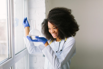 Young beautiful African American girl doctor in a white coat with a stethoscope. sitting near the...
