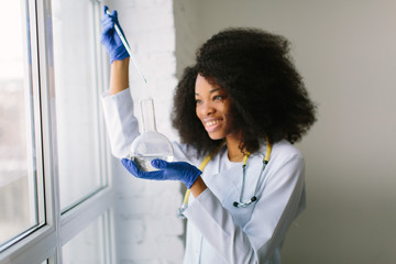 Young beautiful African American girl doctor in a white coat with a stethoscope. sitting near the...
