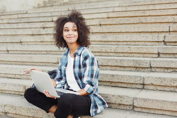 Smiling student sitting on stairs using laptop