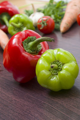 Red tomatoes and green peppers on a table on the background of vegetables. Fresh tomatoes and peppers on a wooden brown table..