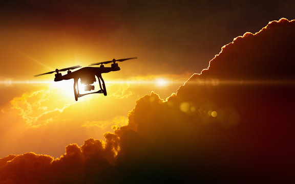 Silhouette of flying drone in glowing red sunset sky
