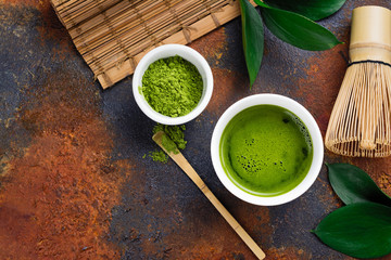 Green matcha tea drink and tea accessories on dark rusty background
